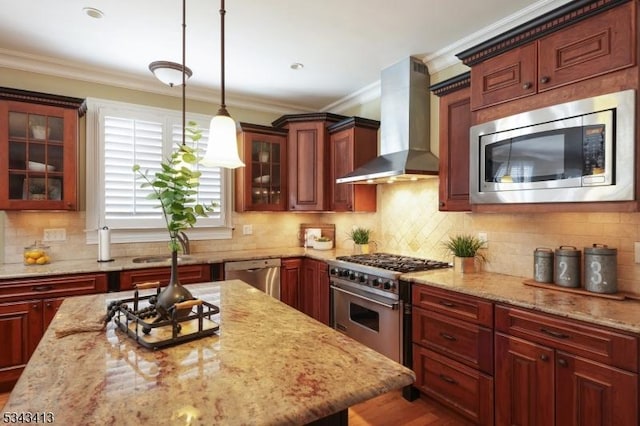 kitchen with appliances with stainless steel finishes, wall chimney exhaust hood, ornamental molding, and hanging light fixtures