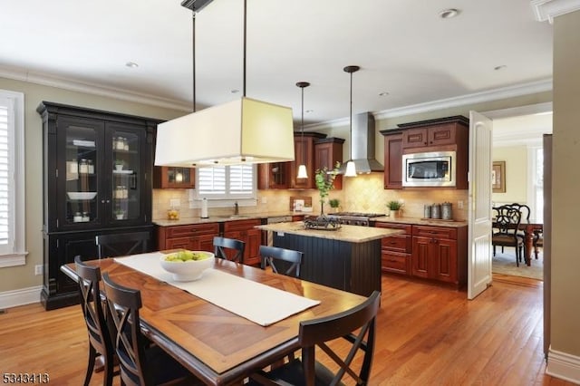 kitchen featuring light wood-style flooring, a sink, stainless steel appliances, wall chimney range hood, and hanging light fixtures