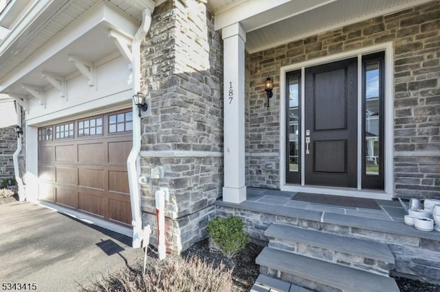 entrance to property featuring a porch, a garage, brick siding, and stone siding