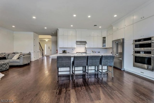 kitchen featuring a breakfast bar, under cabinet range hood, backsplash, appliances with stainless steel finishes, and light countertops