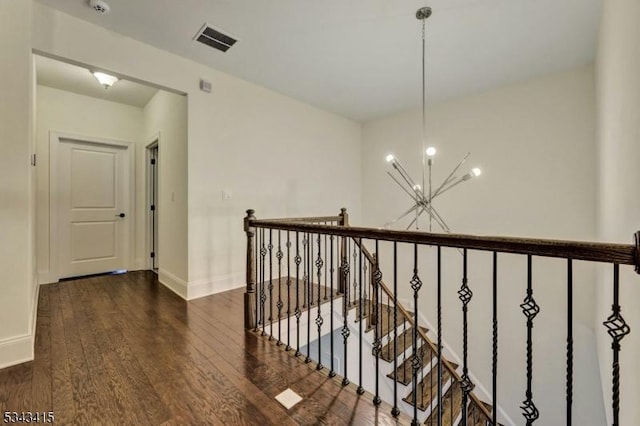 corridor featuring wood finished floors, visible vents, baseboards, an inviting chandelier, and an upstairs landing