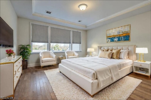 bedroom featuring baseboards, visible vents, ornamental molding, hardwood / wood-style flooring, and a raised ceiling