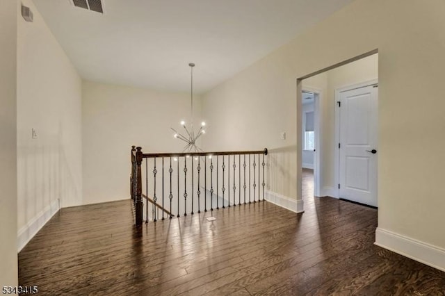 unfurnished room featuring visible vents, baseboards, an inviting chandelier, and hardwood / wood-style flooring