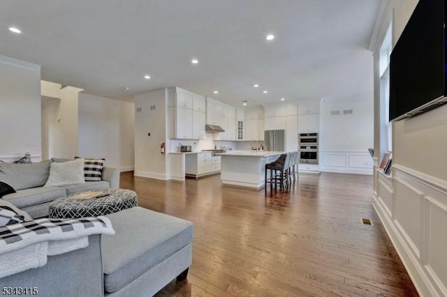 living area featuring visible vents, wainscoting, recessed lighting, a decorative wall, and dark wood-style flooring