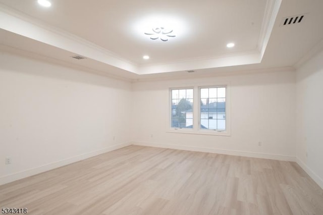 spare room with visible vents, light wood-type flooring, a tray ceiling, and ornamental molding