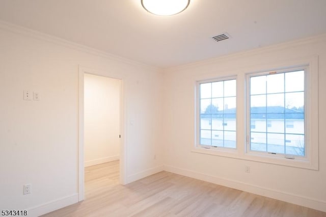 spare room featuring light wood finished floors, visible vents, crown molding, and baseboards