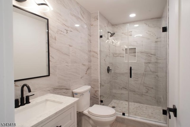 full bath featuring vanity, tile walls, toilet, and a stall shower