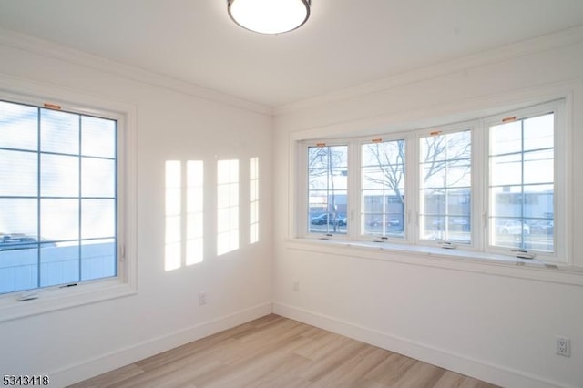 spare room featuring baseboards, plenty of natural light, light wood-style flooring, and crown molding