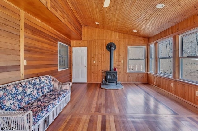 unfurnished living room featuring wood finished floors, wooden ceiling, wood walls, lofted ceiling, and a wood stove