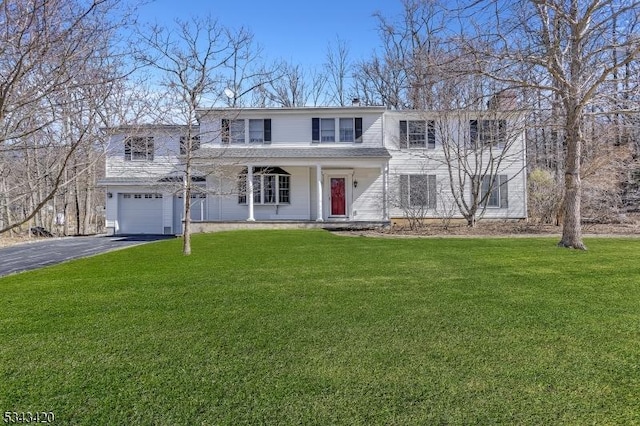 traditional-style house with aphalt driveway, covered porch, an attached garage, and a front yard