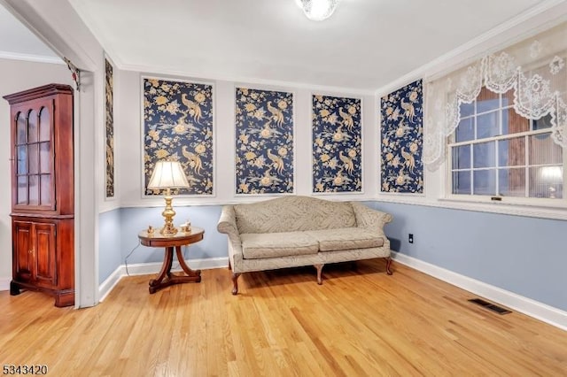 living area featuring baseboards, wood finished floors, visible vents, and ornamental molding