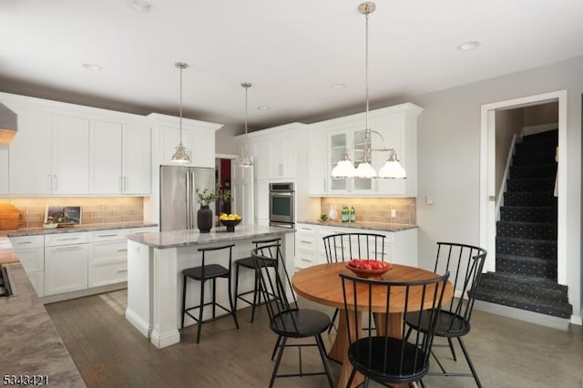 kitchen with a breakfast bar area, a kitchen island, freestanding refrigerator, decorative backsplash, and white cabinetry