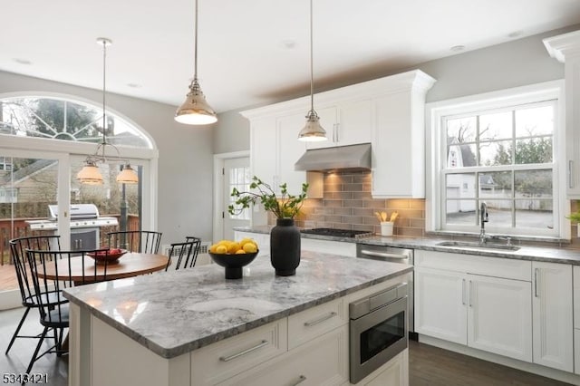 kitchen featuring a kitchen island, under cabinet range hood, decorative backsplash, appliances with stainless steel finishes, and a sink