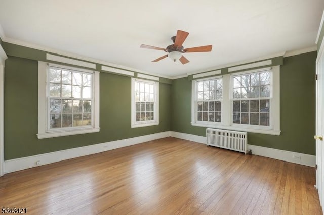 spare room featuring a ceiling fan, hardwood / wood-style flooring, radiator heating unit, crown molding, and baseboards