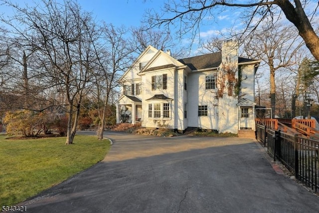 view of front of property featuring aphalt driveway, a front lawn, a chimney, and fence