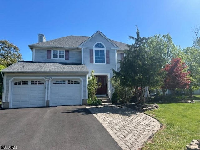 traditional home featuring a chimney, a front yard, aphalt driveway, and an attached garage
