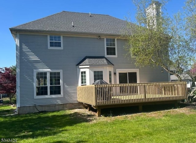 rear view of house with a shingled roof, a yard, a chimney, and a deck