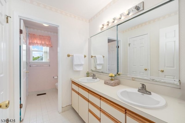 full bath with toilet, double vanity, and baseboards