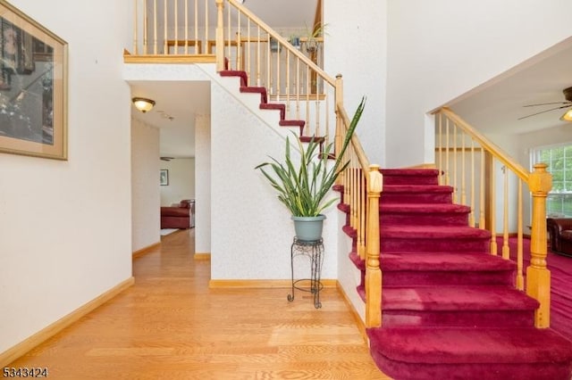 staircase with wood finished floors, a ceiling fan, and baseboards