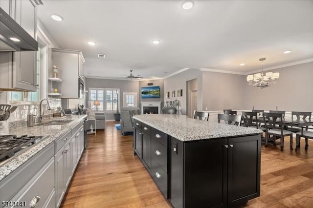 kitchen featuring dark cabinetry, a kitchen island, a sink, under cabinet range hood, and ceiling fan with notable chandelier