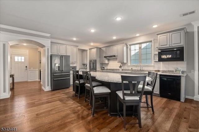 kitchen with black appliances, a breakfast bar, a sink, a center island, and arched walkways