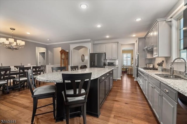 kitchen featuring a center island, under cabinet range hood, wood finished floors, stainless steel appliances, and a sink