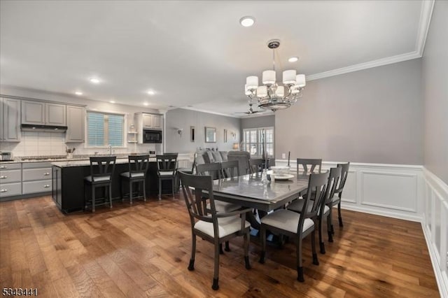 dining room featuring crown molding, dark wood finished floors, a wainscoted wall, recessed lighting, and a notable chandelier