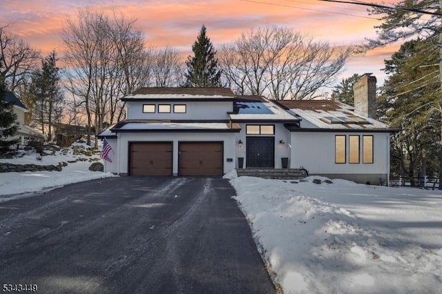 view of front facade with aphalt driveway, a garage, and a chimney