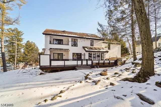 snow covered back of property with a wooden deck, a balcony, and stucco siding