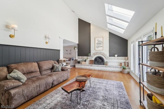 living area with a fireplace, a skylight, wood finished floors, and high vaulted ceiling