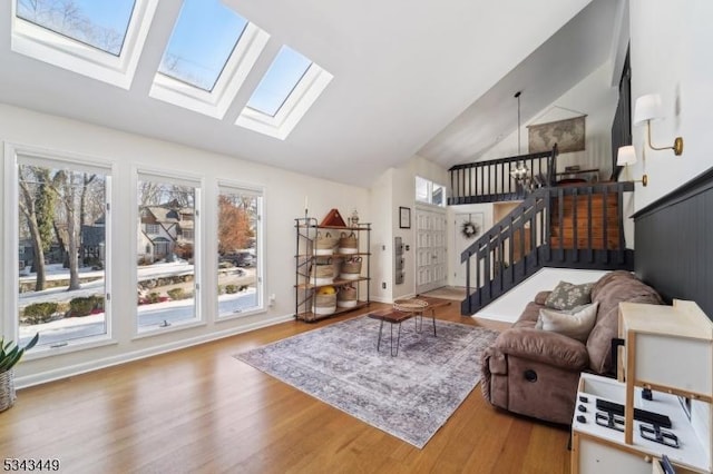 living area with baseboards, lofted ceiling with skylight, wood finished floors, and stairs