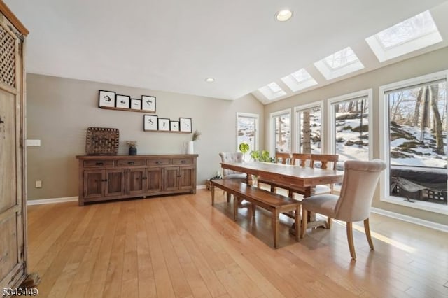 dining space with lofted ceiling with skylight, light wood-style flooring, and a healthy amount of sunlight