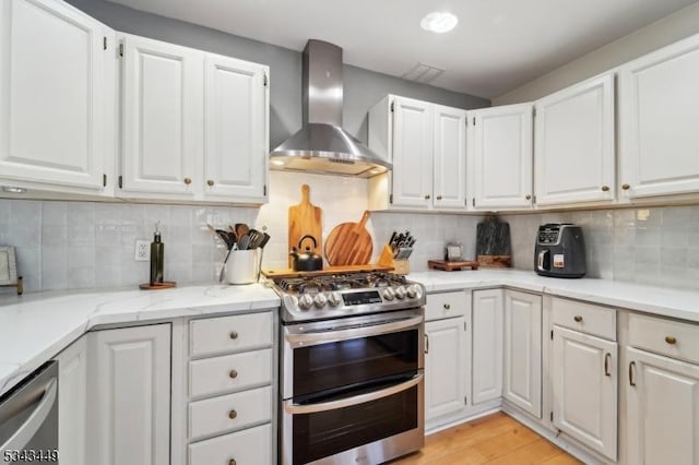 kitchen featuring stainless steel appliances, white cabinetry, and wall chimney range hood