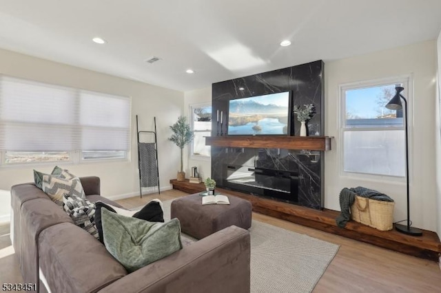 living area featuring visible vents, wood finished floors, recessed lighting, a premium fireplace, and baseboards