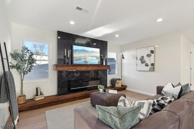 living room featuring recessed lighting, visible vents, wood finished floors, and a high end fireplace