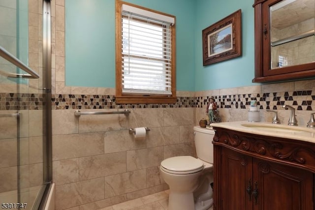 bathroom with tile patterned flooring, toilet, vanity, wainscoting, and tile walls