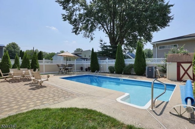 view of pool featuring an outbuilding, a storage shed, a fenced backyard, and a patio area