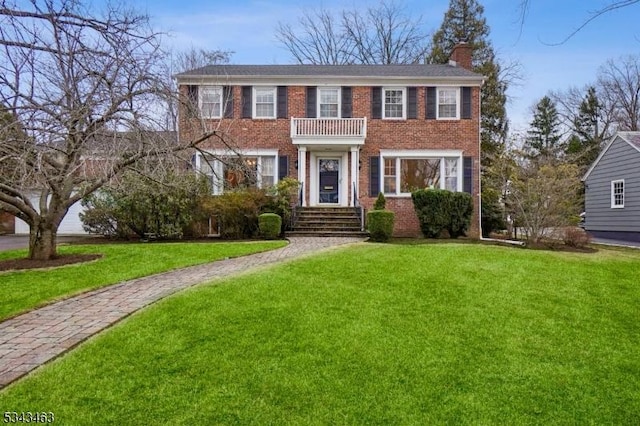 view of front of home with brick siding, a balcony, a chimney, and a front yard