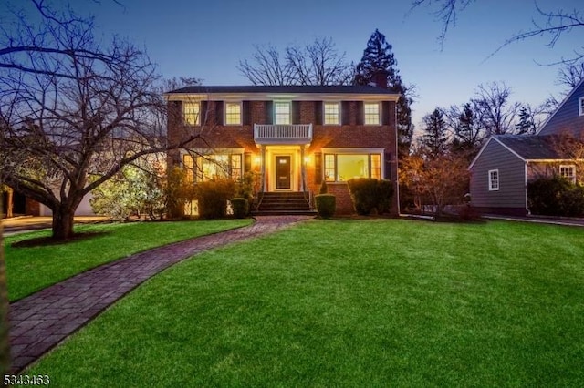 view of front of home with brick siding, a lawn, a chimney, and a balcony