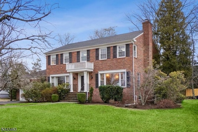 view of front of house featuring brick siding, a front lawn, a balcony, and a chimney