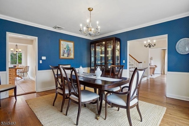 dining room featuring visible vents, wallpapered walls, a chandelier, ornamental molding, and wood finished floors