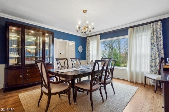 dining room with crown molding, light wood-style floors, and an inviting chandelier