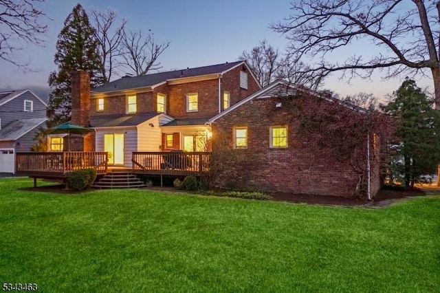 back of house featuring a yard, brick siding, a wooden deck, and a chimney