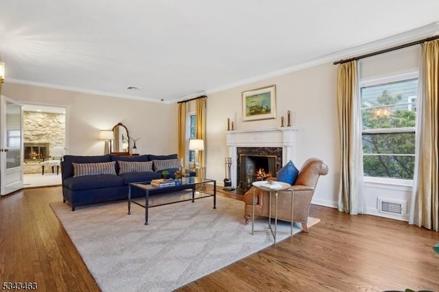 living area with wood finished floors, baseboards, visible vents, a premium fireplace, and crown molding