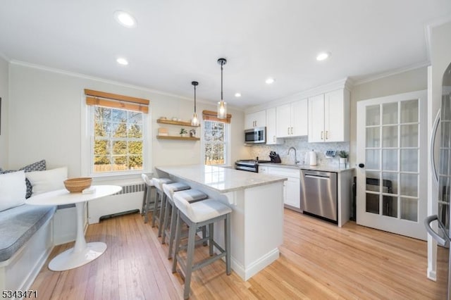 kitchen featuring a breakfast bar, breakfast area, radiator heating unit, white cabinets, and stainless steel appliances