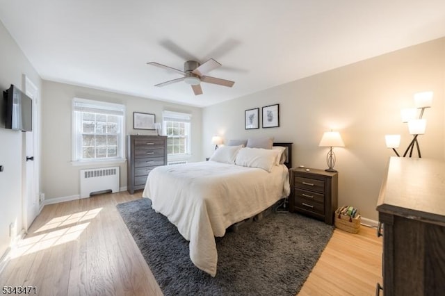 bedroom featuring light wood-type flooring, baseboards, ceiling fan, and radiator heating unit