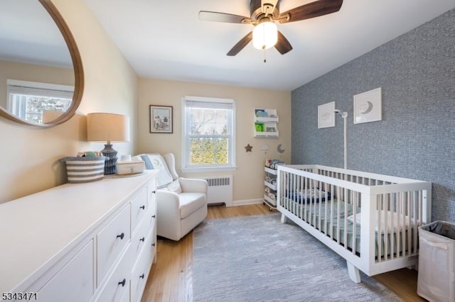 bedroom featuring light wood finished floors, wallpapered walls, an accent wall, radiator heating unit, and a nursery area