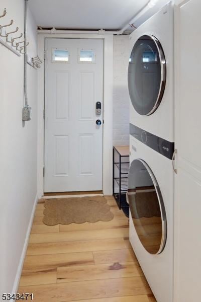 laundry room with light wood finished floors, laundry area, stacked washer / drying machine, and baseboards