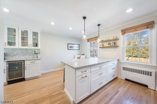 kitchen featuring beverage cooler, light wood-type flooring, radiator heating unit, a peninsula, and white cabinets