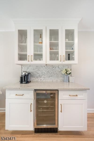 bar featuring backsplash, crown molding, baseboards, wine cooler, and light wood-type flooring